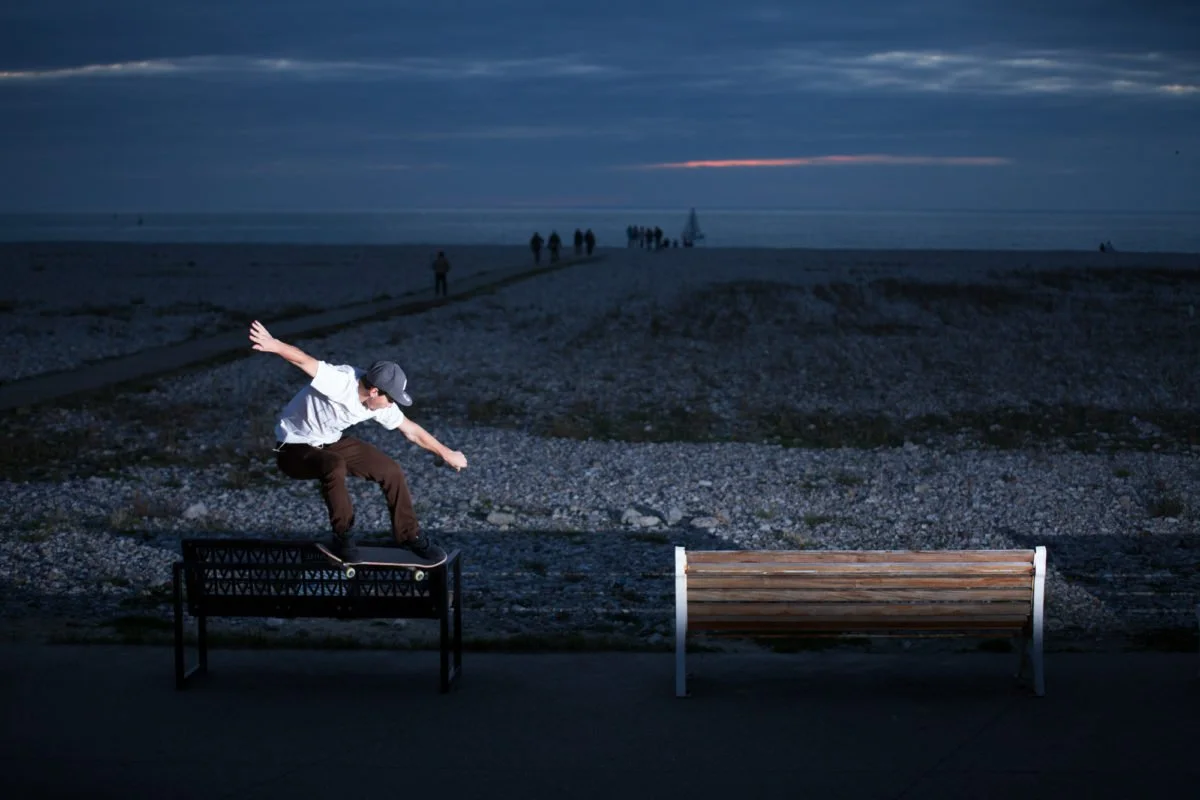 Joseph Garbaccio en skateboard sur un banc de parc la nuit, avec l'océan en arrière-plan et un ciel nuageux.