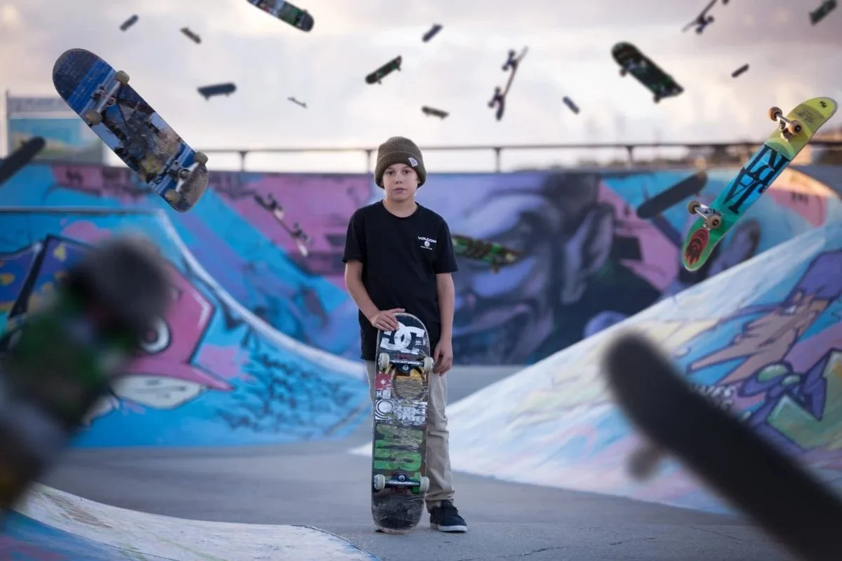 Jeune garçon avec un skateboard à la main dans un skatepark couvert de graffitis, des planches de skateboard volantes dans l'air