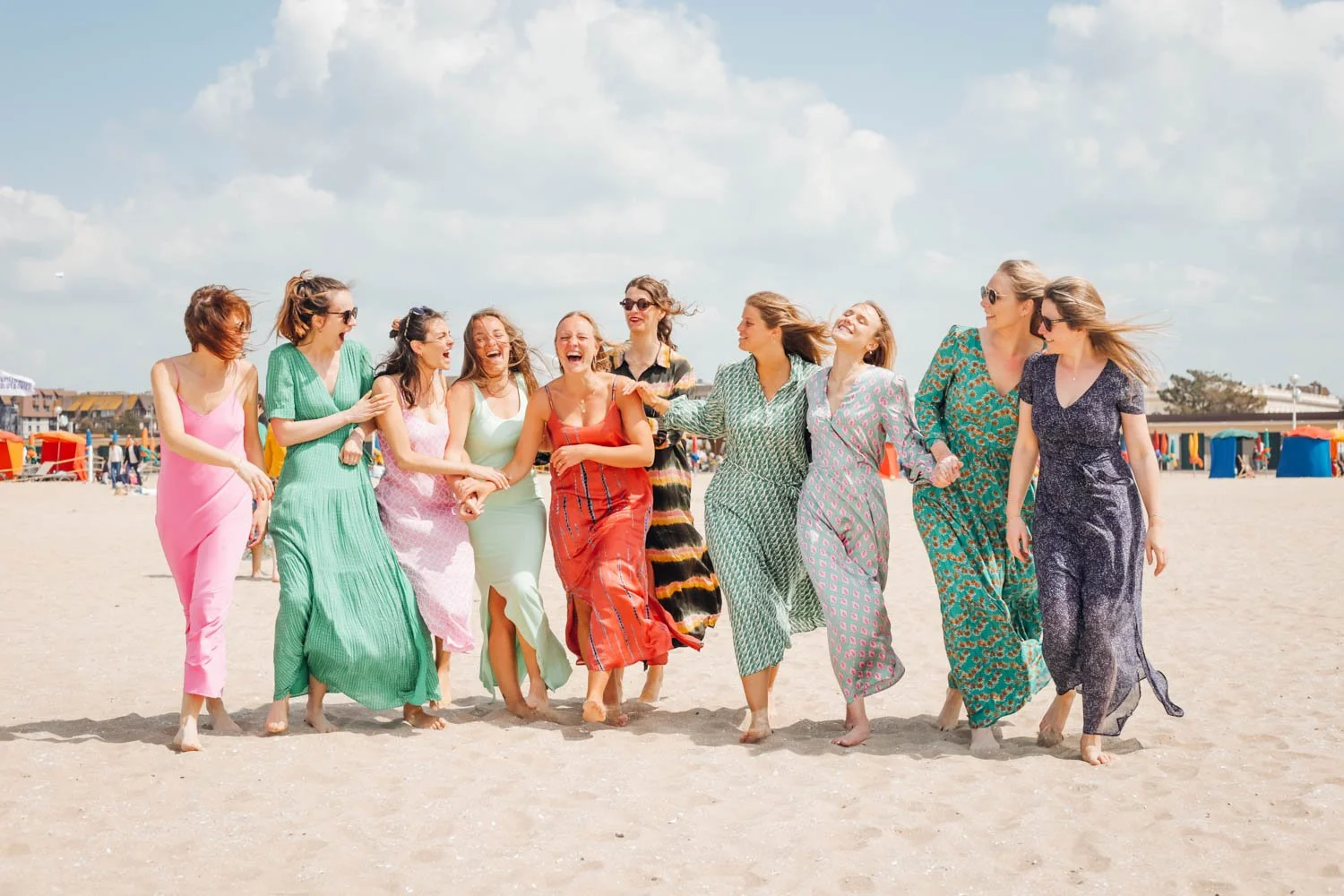 Groupe de femmes souriantes marchant ensemble sur la plage par une journée ensoleillée, vêtues de robes colorées