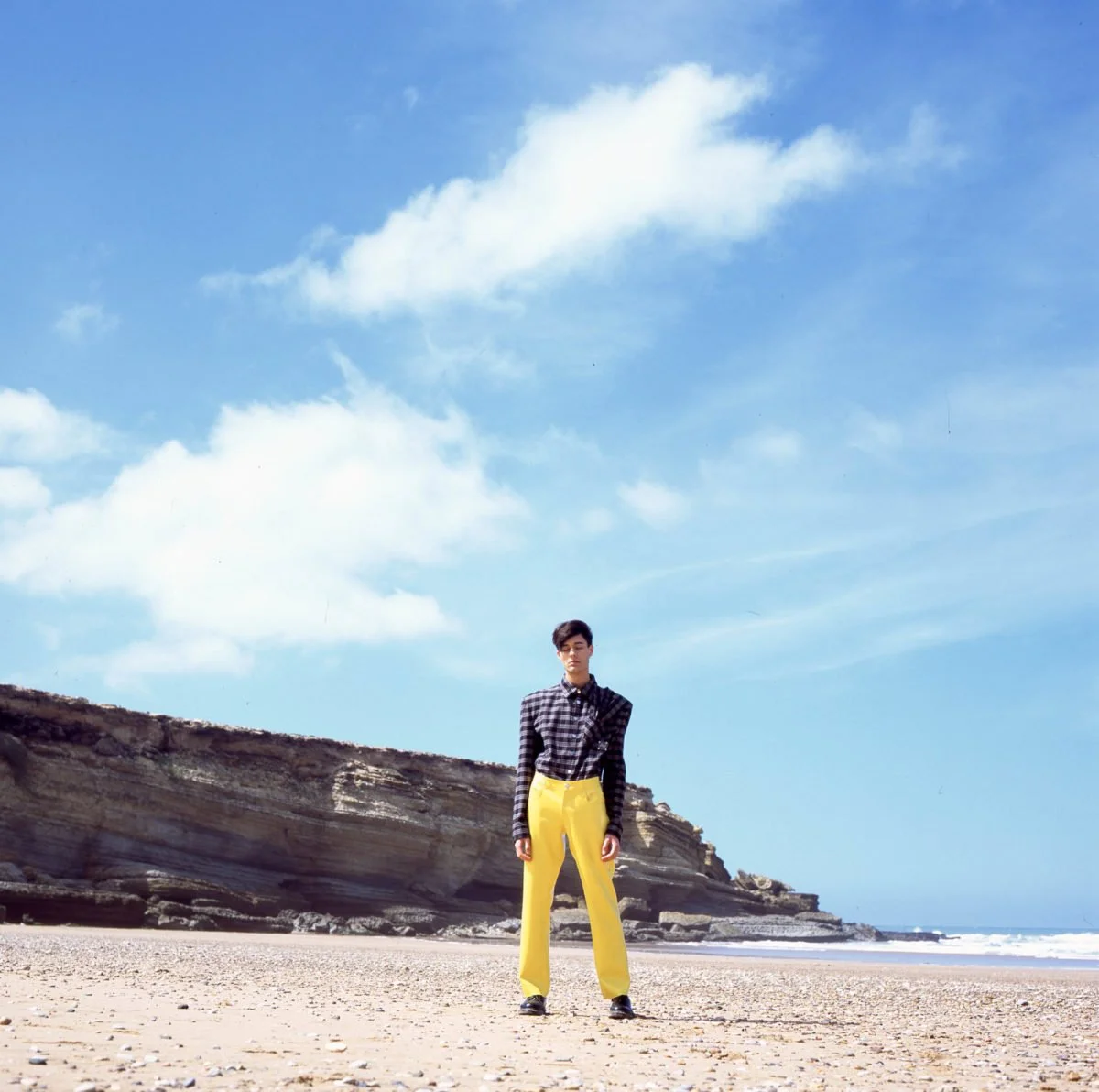 Une personne debout sur une plage avec des falaises en arrière-plan et un ciel bleu avec quelques nuages. Arthur Avellano