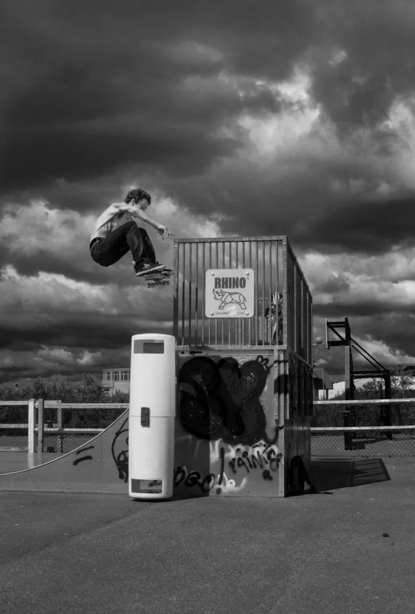 Jeune garçon faisant un saut en skateboard à Deauville au-dessus d'une structure de skate avec un ciel orageux en arrière-plan.