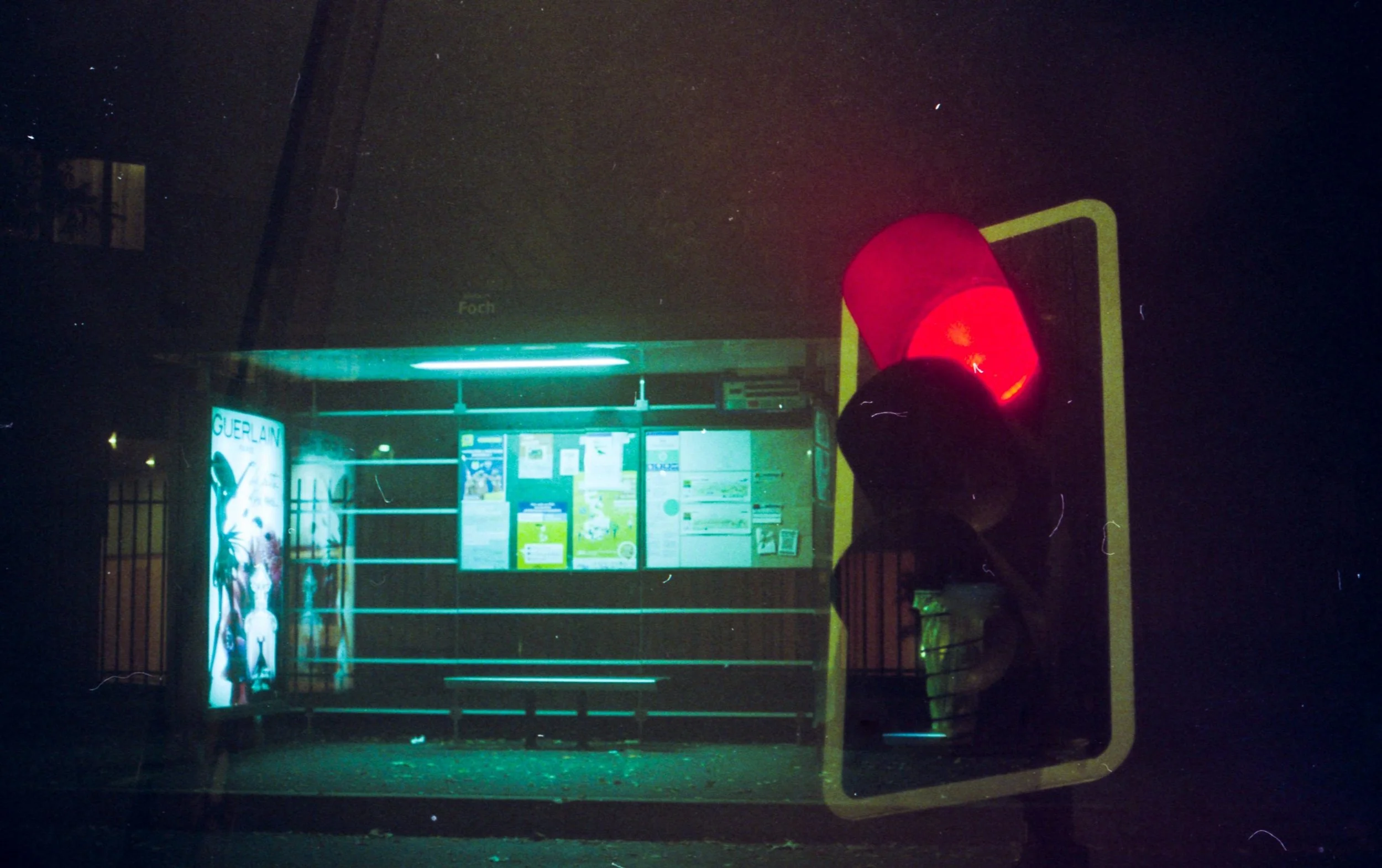 Un panneau d'information d'une station de bus ou de métro sous une lumière verte et violette, avec un affichage lumineux et une figurine humaine en vitrine.