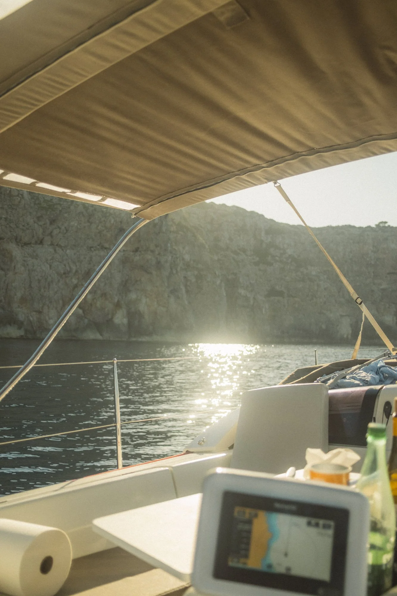 Vue depuis un bateau avec une toile pare-soleil, une mer calme, un rocher en arrière-plan, des instruments de navigation et des objets personnels sur le bateau à majorque