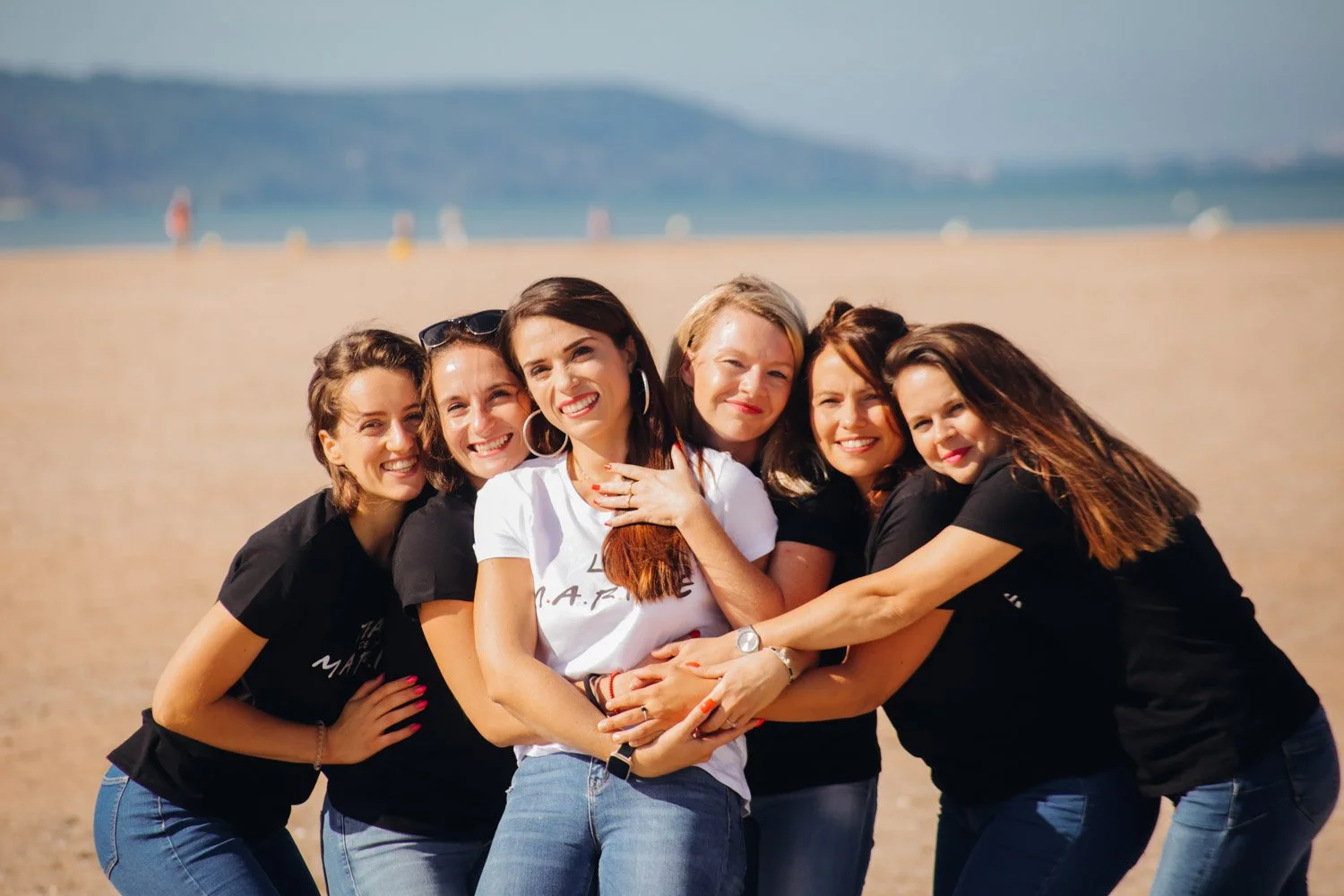 Groupe de six jeunes femmes souriantes embrassant lors d'une journée ensoleillée à la plage pour un EVJF