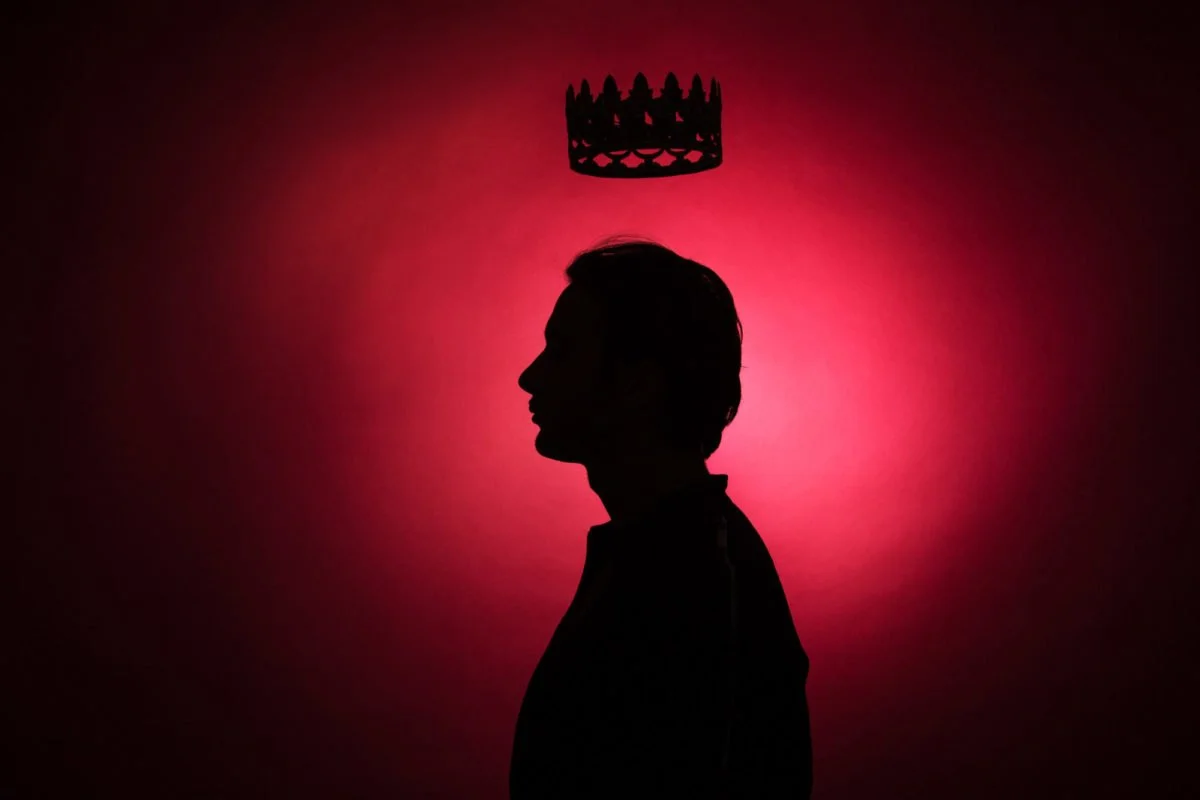 Lord Esperanza devant un fond rouge avec une couronne noire suspendue au plafond.