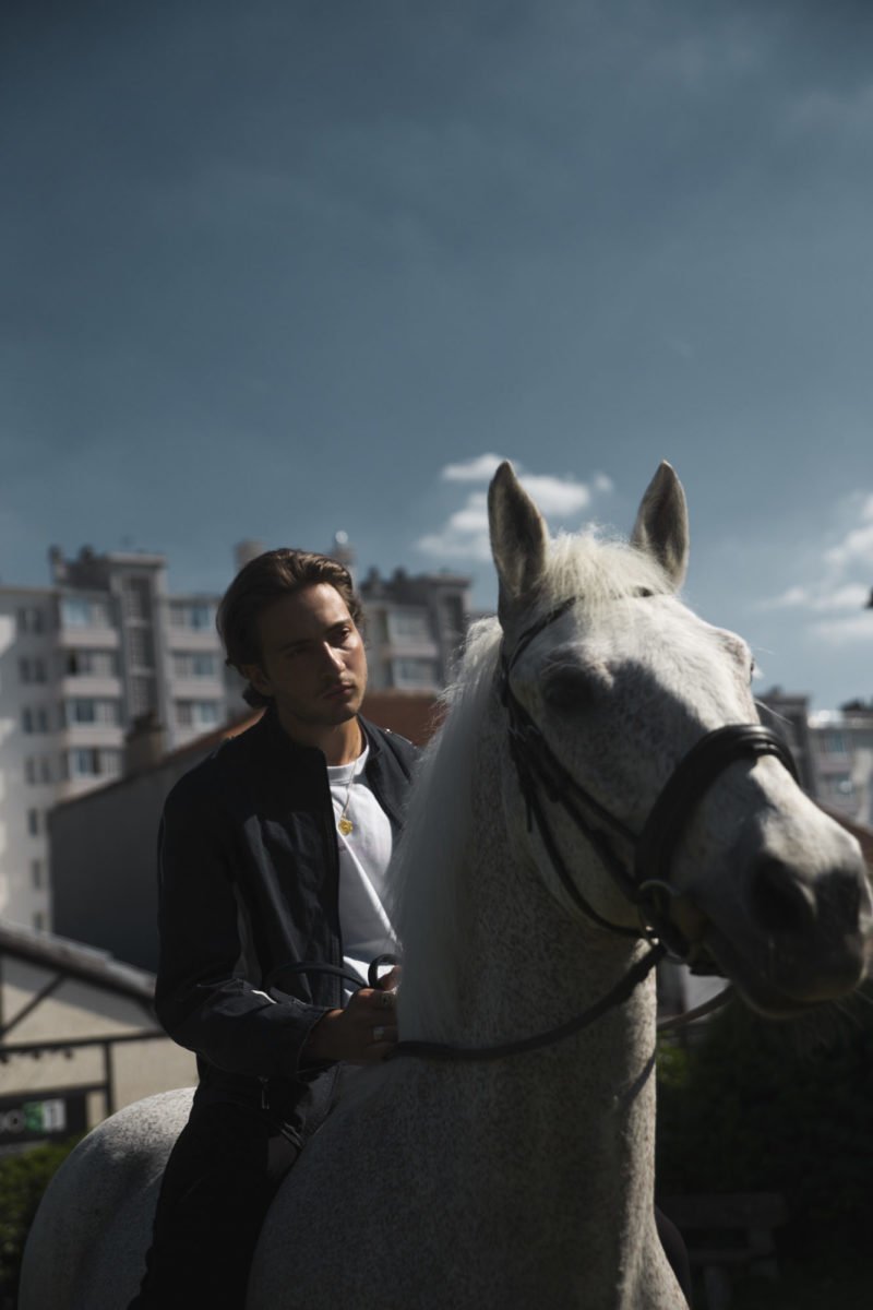 Lord esperanza assis sur un cheval blanc dans un environnement urbain avec des bâtiments sous un ciel bleu avec quelques nuages.