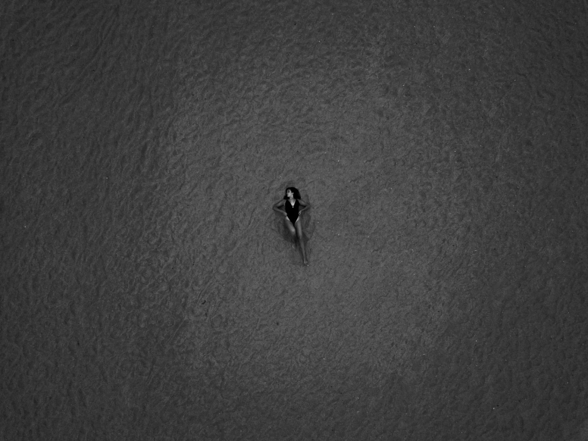 Une femme en maillot de bain allongée sur la plage noire vu d'en haut.