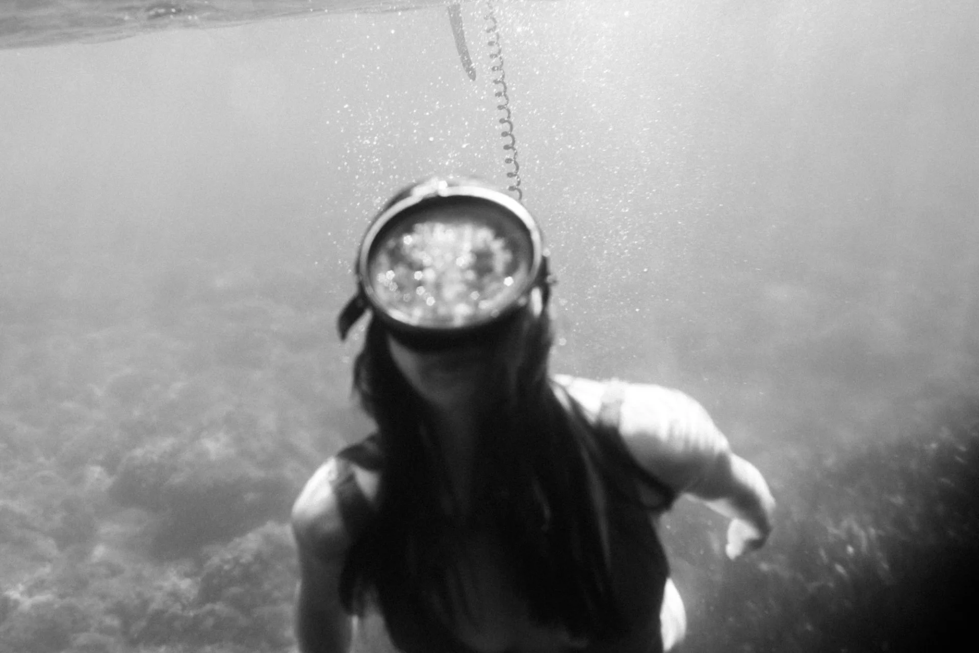 	
Une femme nage sous l'eau, portant un masque de plongée et une combinaison de natation, avec une vue claire de l'océan ou de la mer.