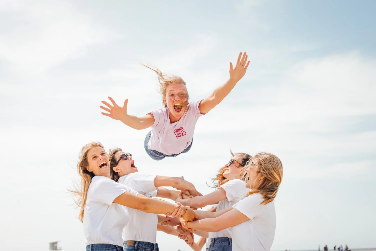 Un groupe de femmes qui se tiennent par les mains, en train de supporter une femme qui fait un saut dans les airs, au ciel clair.