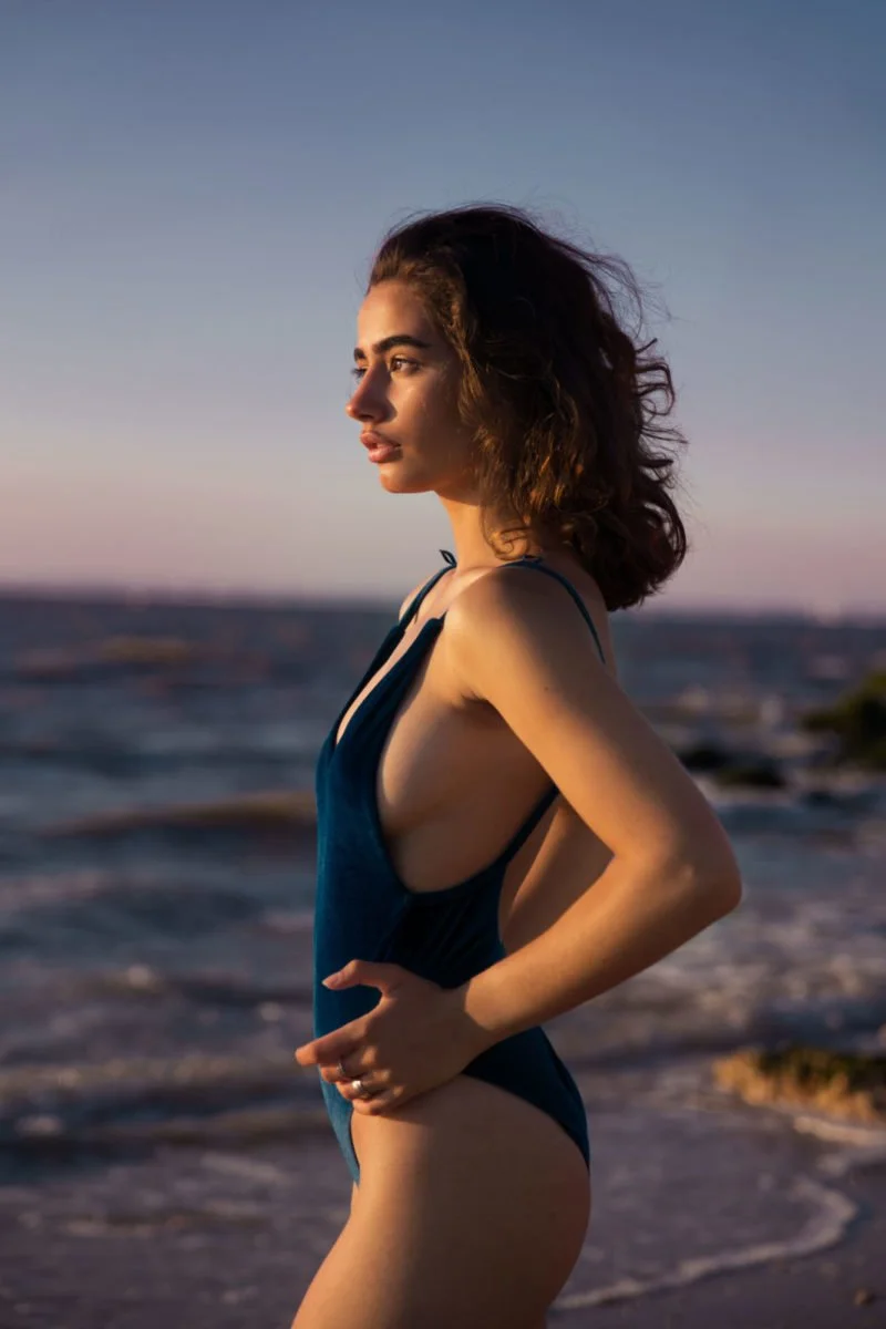 Une femme en maillot de bain debout sur la plage lors du coucher du soleil