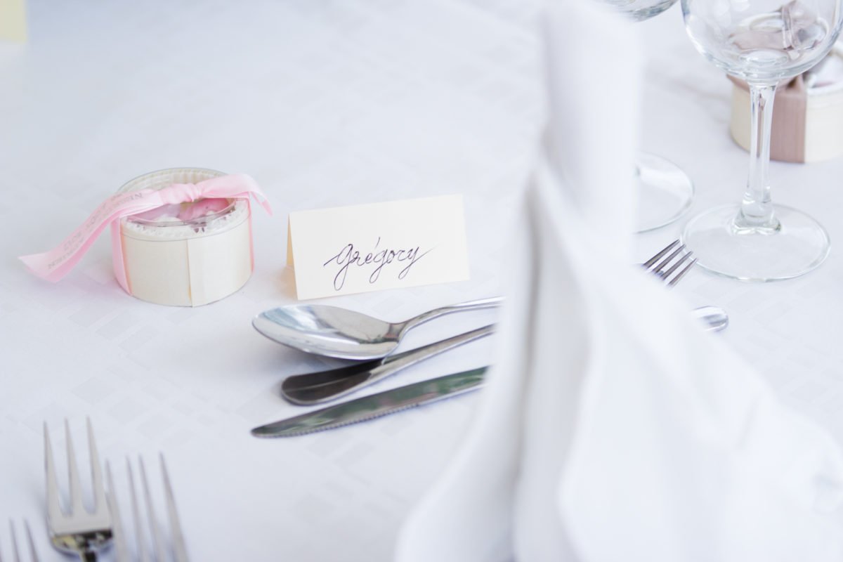 Table de mariage avec un nom 'Gregory', couverts, verre à vin, et un petit cadeau emballé avec un ruban rose.