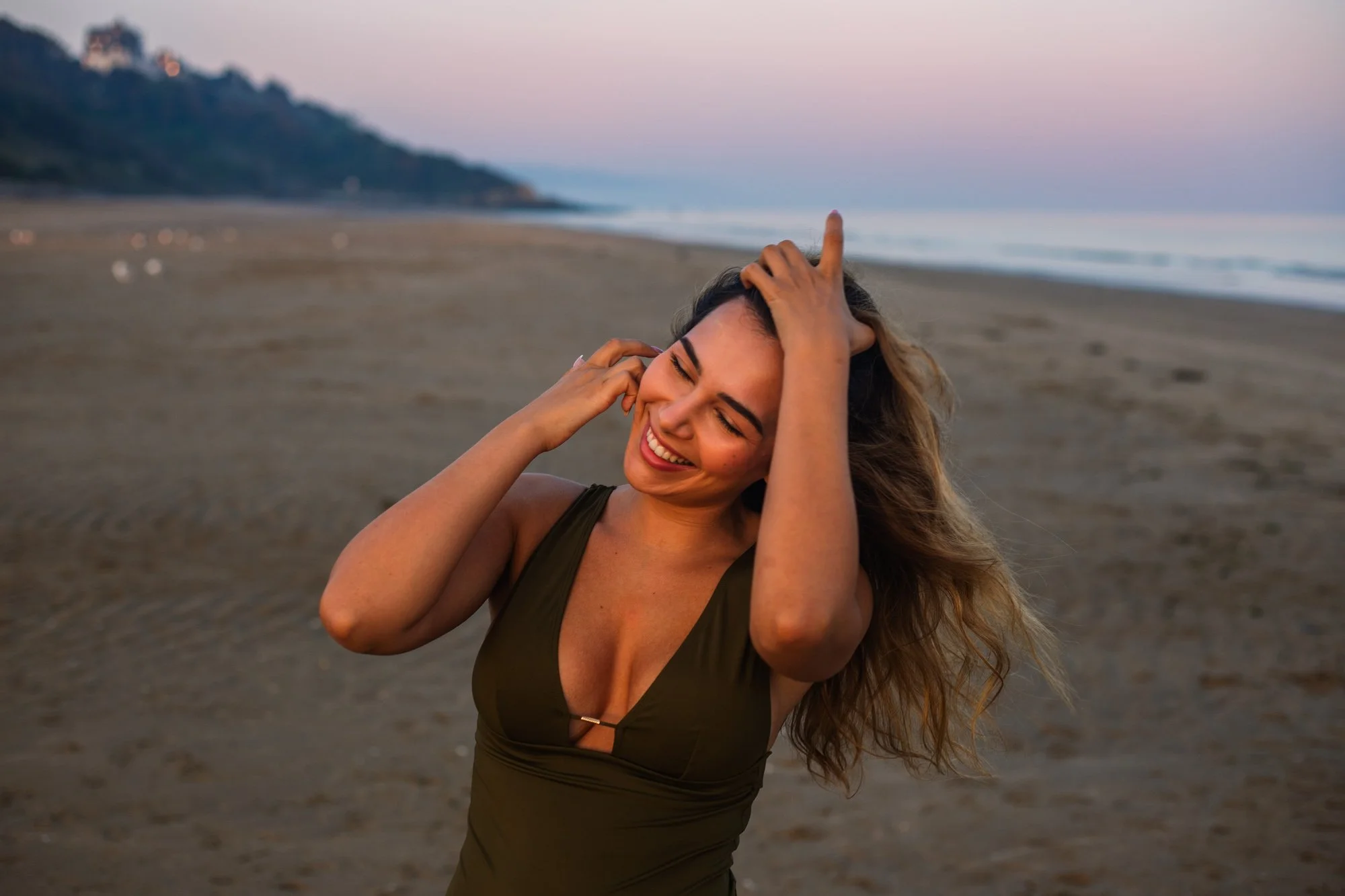 Jeune femme souriante à la plage, expression de bonheur, cheveux longs, robe verte, soirée ou coucher de soleil.