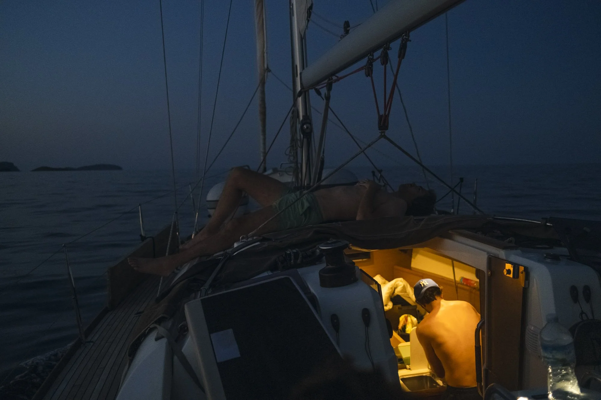 Une personne allongée sur un bateau au crépuscule ou la nuit, avec un intérieur illuminé, en train de se préparer ou de vérifier quelque chose à l'intérieur du bateau à majorque