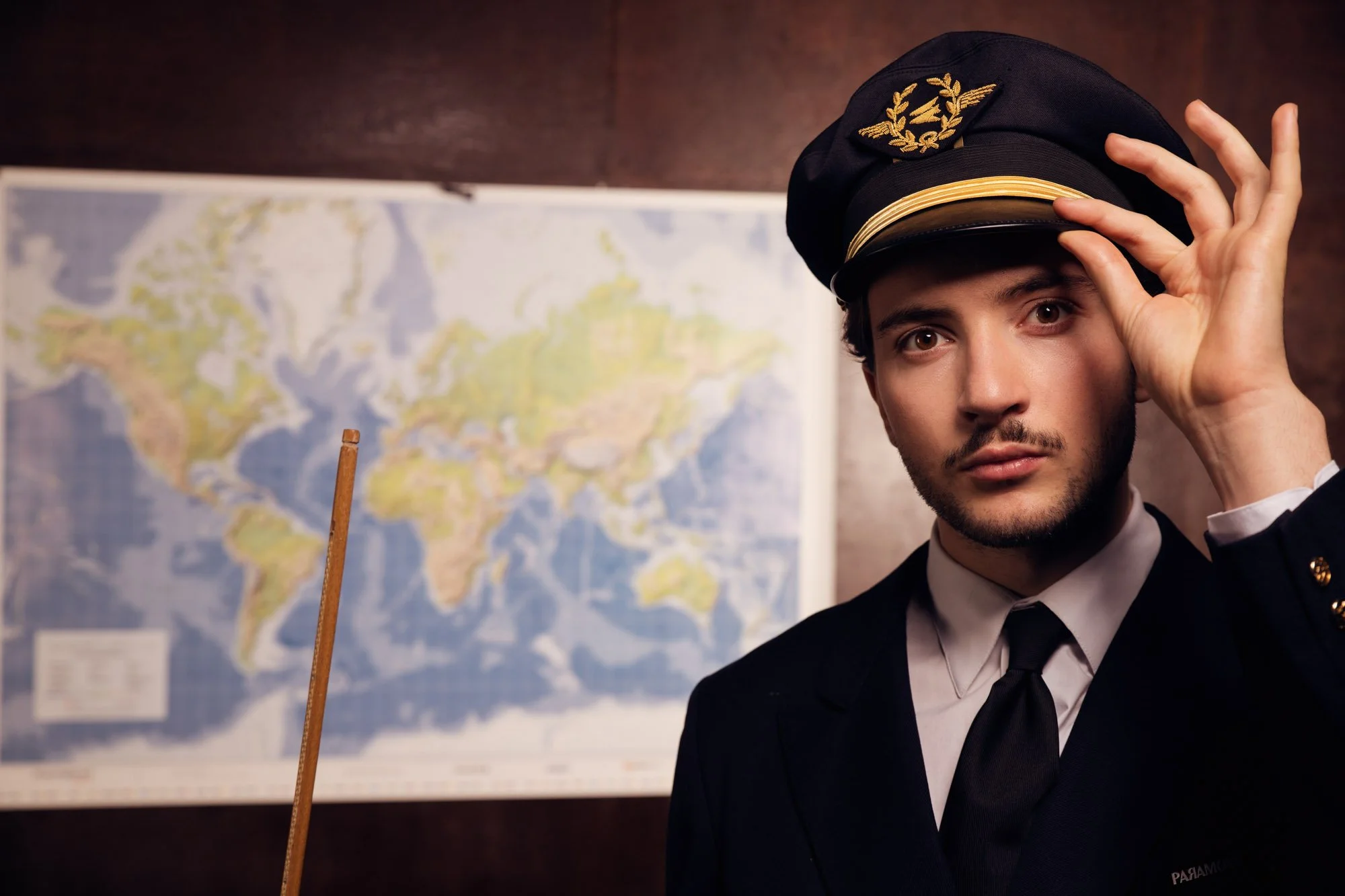 Lord Esperanza en uniforme de capitaine de navire ajuste son chapeau en regardant l'appareil photo. Il y a une carte du monde en arrière-plan.