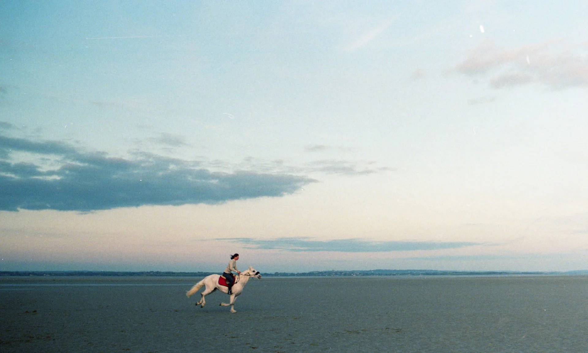 Une personne cavalant à cheval sur une plage avec un ciel nuageux
