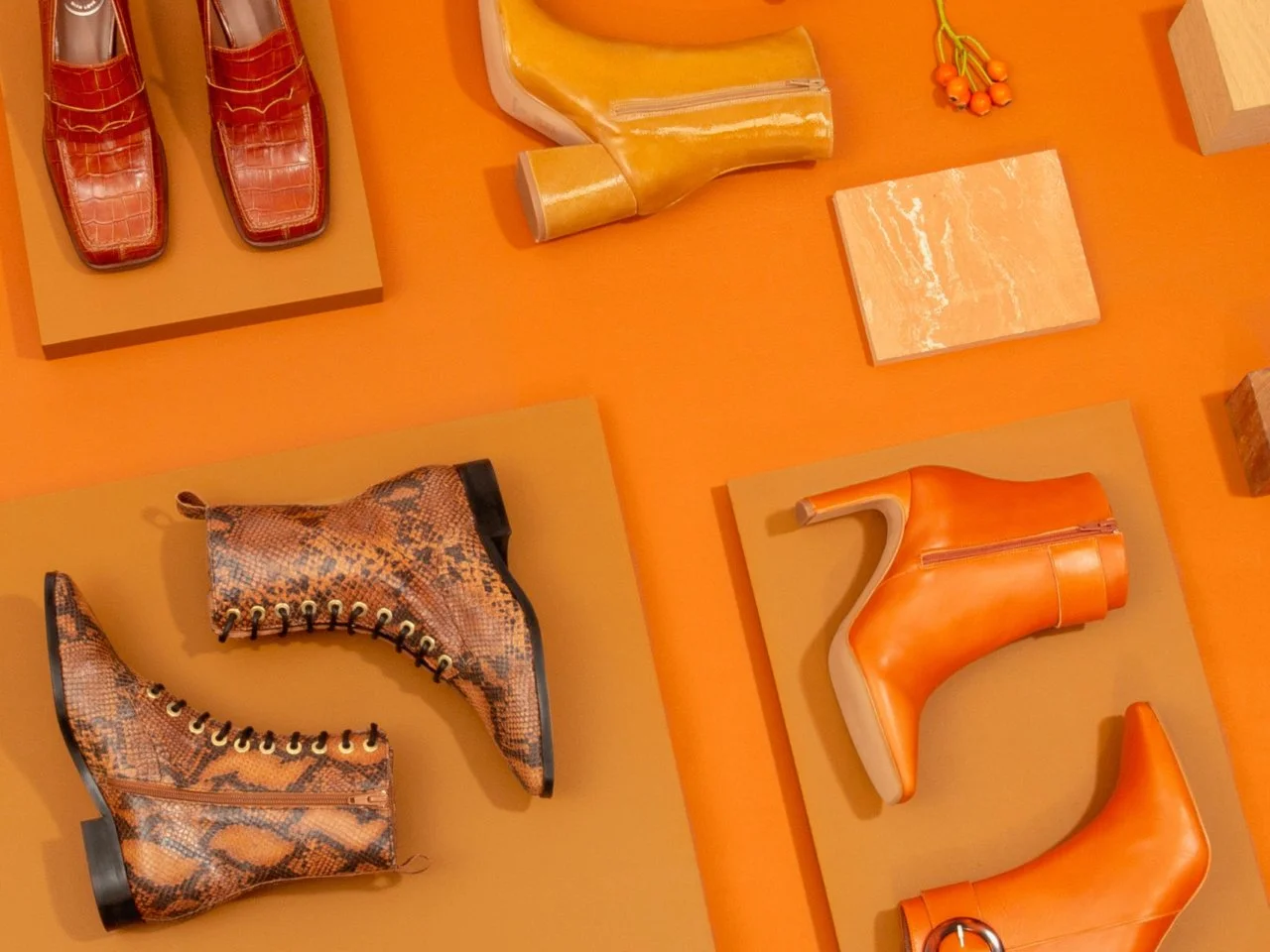 Chaussures à talons de différentes couleurs et textures, dont une paire en cuir orange et une paire en cuir à motif serpent, sur une surface orange. Sarenza