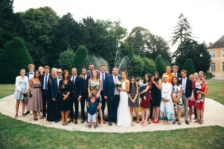 Groupe de personnes lors d'un mariage dans un jardin avec des arbres et un bâtiment en arrière-plan.