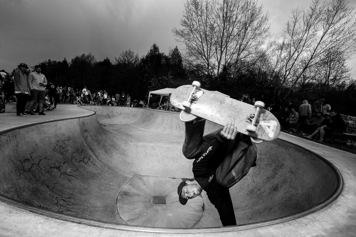 Un skateur effectuant une manœuvre dans un bowl de skatepark avec un public qui regarde.