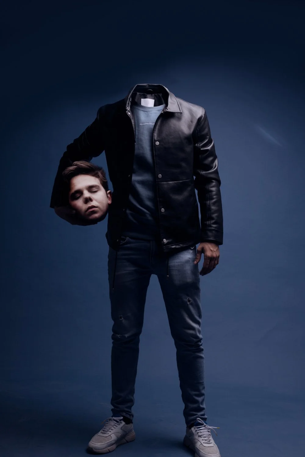 2THportant une veste en cuir et un jean déchiré, tenant une tête de poupée ou une effigie de visage humain avec des yeux fermés, dans un environnement sombre et dramatique.