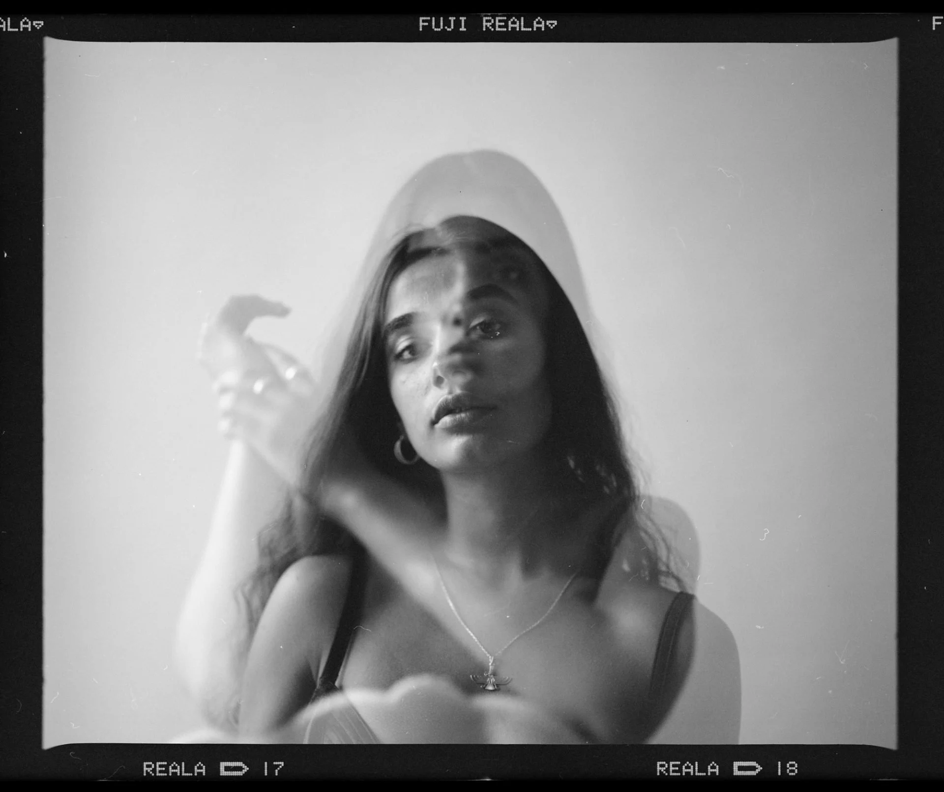 Un autoportrait noir et blanc d'une femme avec de longs cheveux et des boucles d'oreilles, prise avec un appareil photo vintage dans un style rétro.
