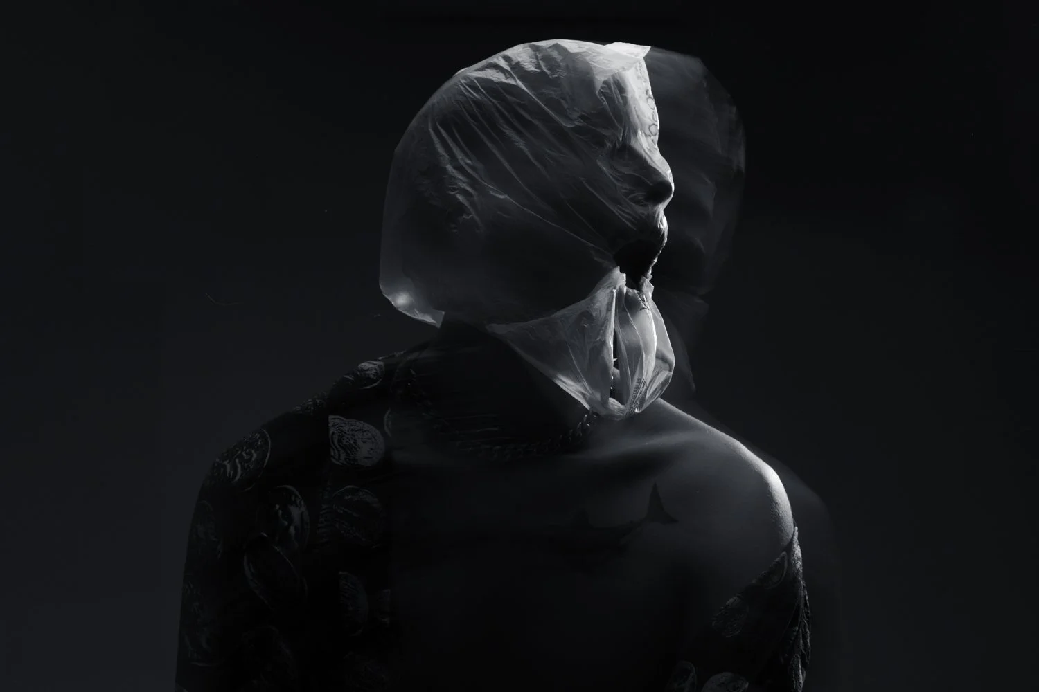 Un portrait artistique en noir et blanc d'une personne avec un visage partiellement couvert d'un plastique transparent, et une peau claire, avec des tatouages sur l'épaule.