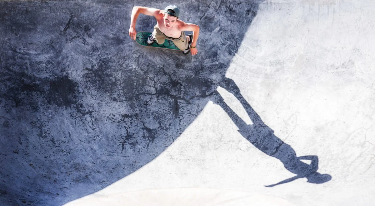 Un garçon en skateboard vu du dessus dans un skatepark, avec son ombre projetée sur le sol.