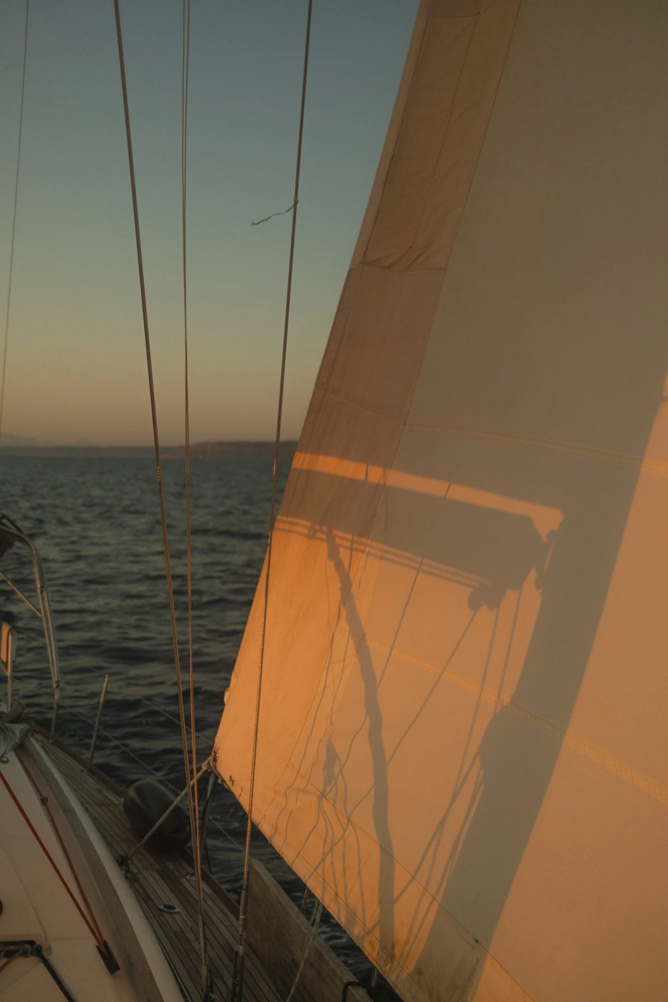 Coucher de soleil sur la mer vu depuis un bateau, avec une voile orange projetant une ombre sur la surface de l'eau.