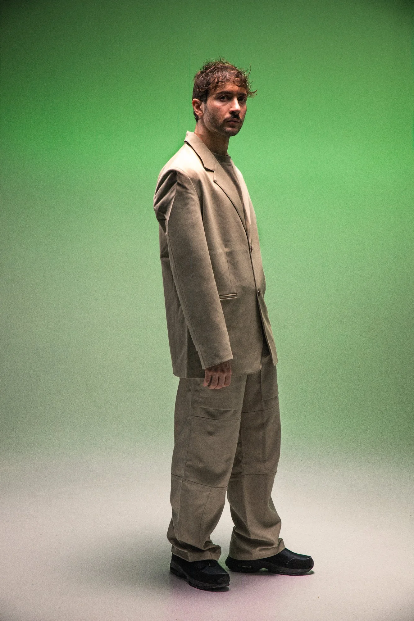 Homme en vêtements beige, debout devant un fond vert.