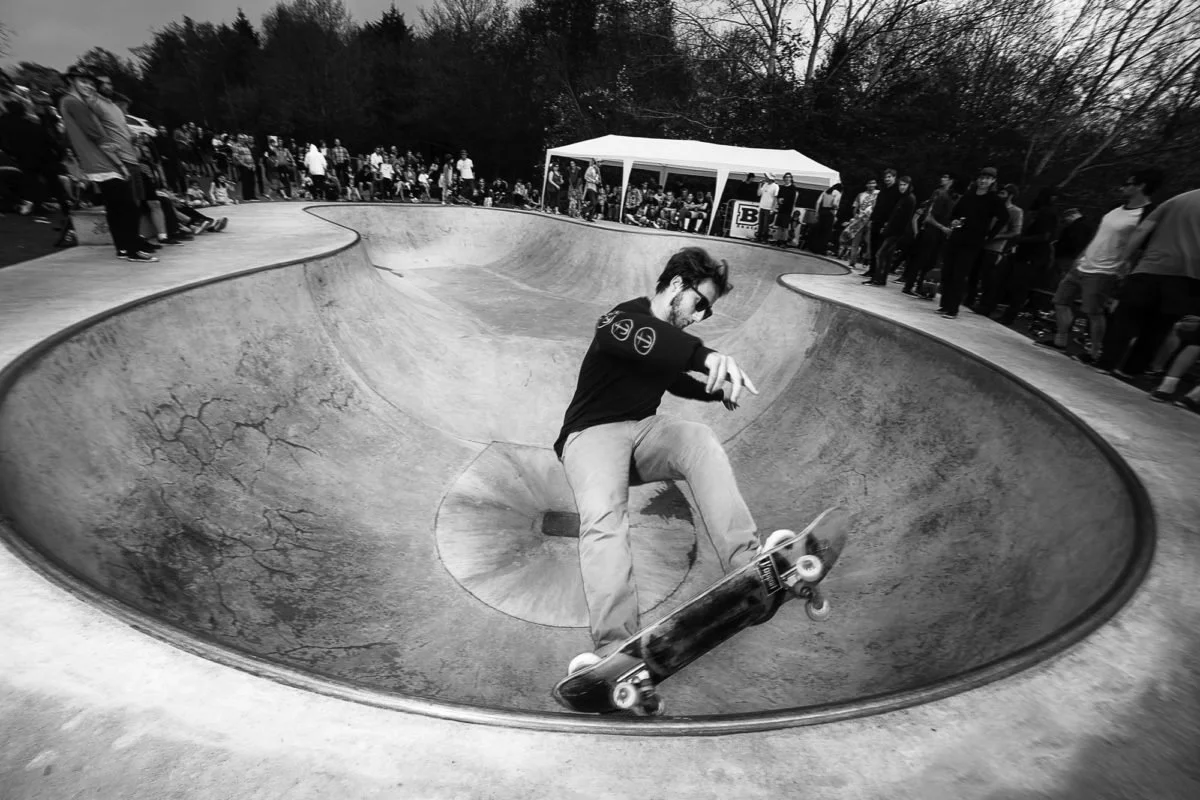 Skateur effectuant une manoeuvre dans un bowl de skatepark, entouré de spectateurs.