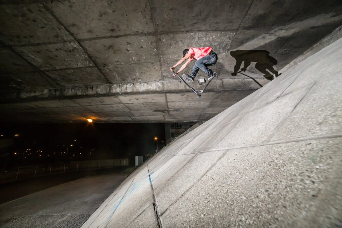 Jeune homme faisant du trick en scooter dans une zone urbaine la nuit, sous un pont ou un espace de béton.