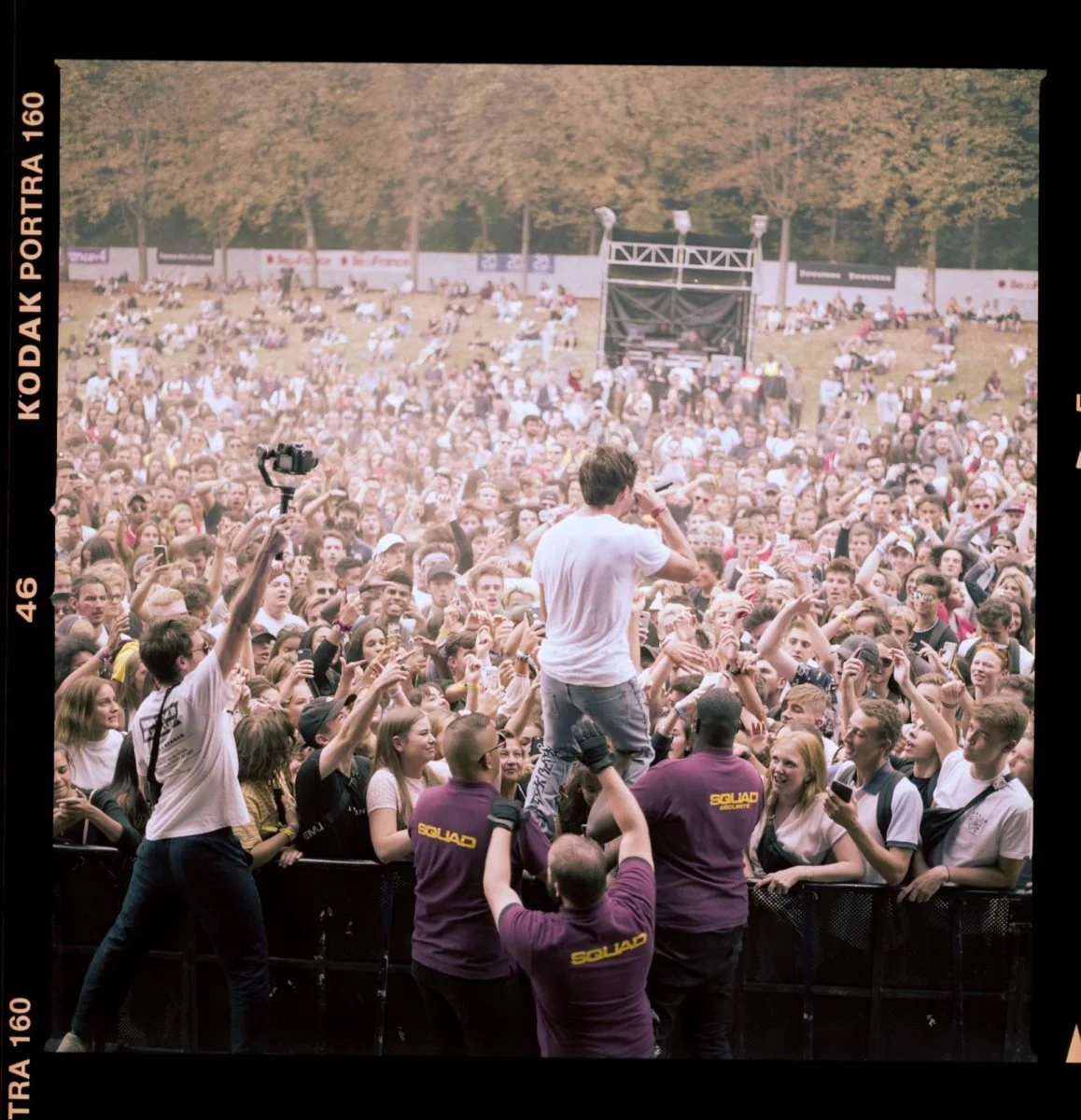 Un artiste en blanc chante lors d'un concert devant une foule immense dans un parc.
