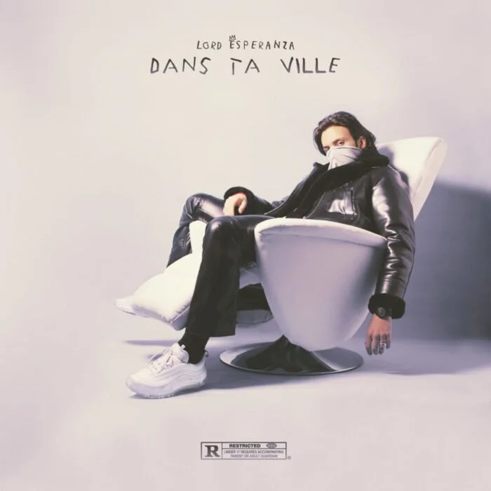 Une personne portant un masque et une veste en cuir noir est assise dans un fauteuil blanc futuriste. Des écritures en français, 'Lord Espérance dans ta ville', sont au-dessus de la personne. Une étiquette de classification 'Restricted' est en bas de