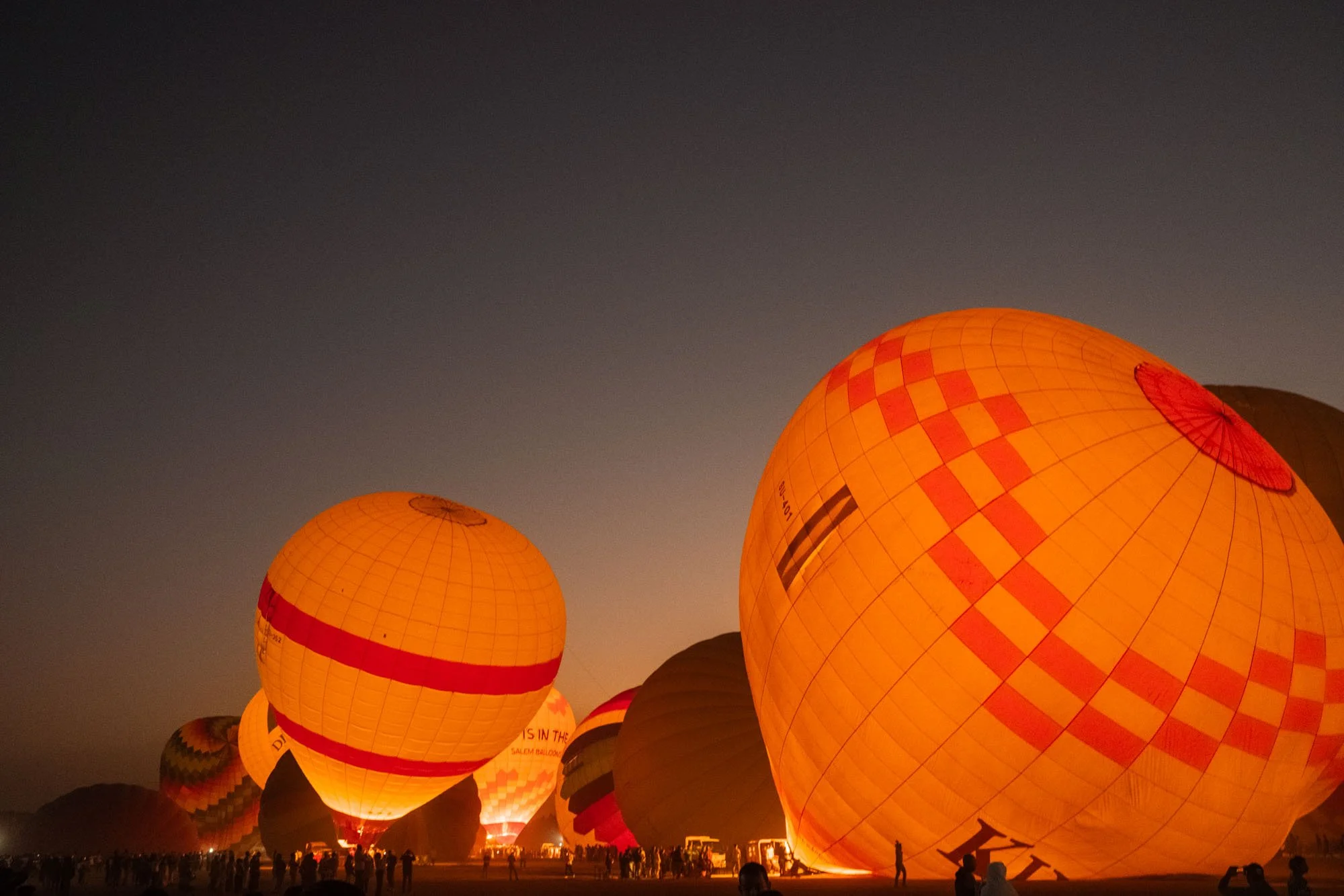 Ballons lumineux orange dans le ciel crépusculaire lors d'un festival, avec une foule en dessous en egypte