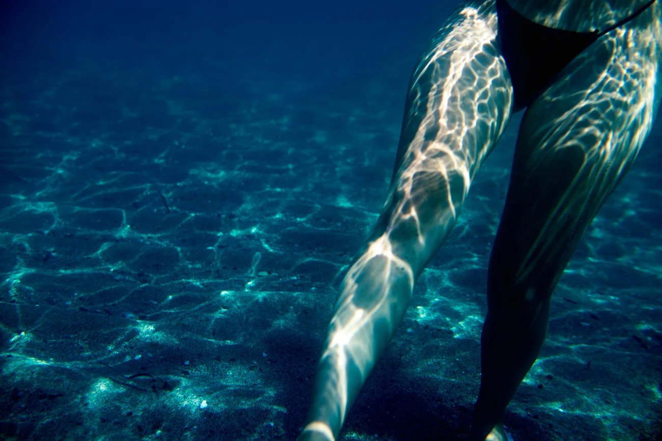 Un plongeur ou nageur sous l'eau, capturant la lumière sur ses jambes dans une piscine ou un environnement aquatique.