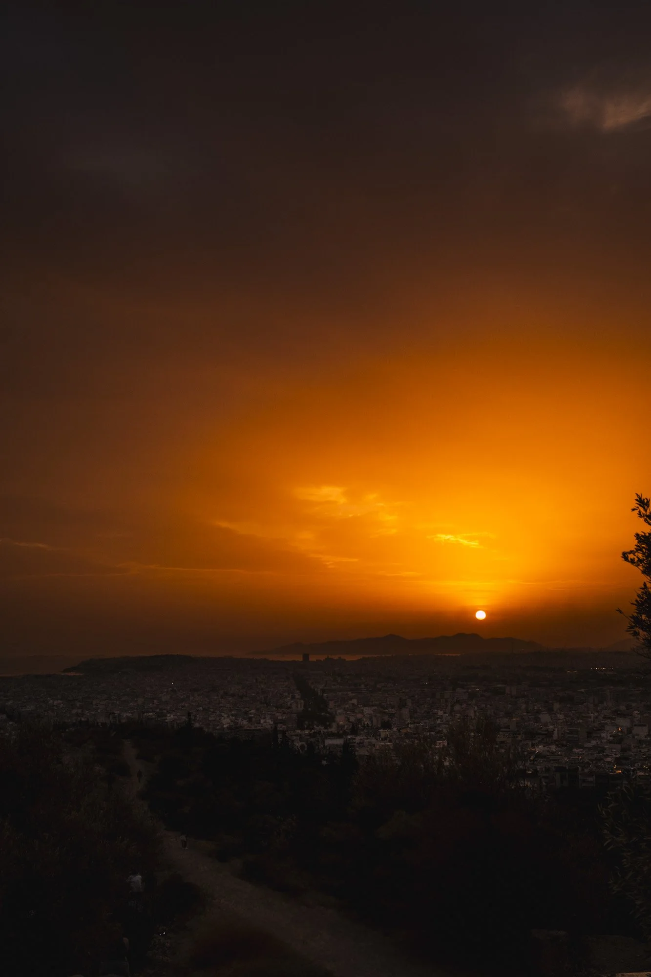 Coucher de soleil sur une ville côtière avec des montagnes à l'arrière-plan, ciel coloré en orange et noir à athenes