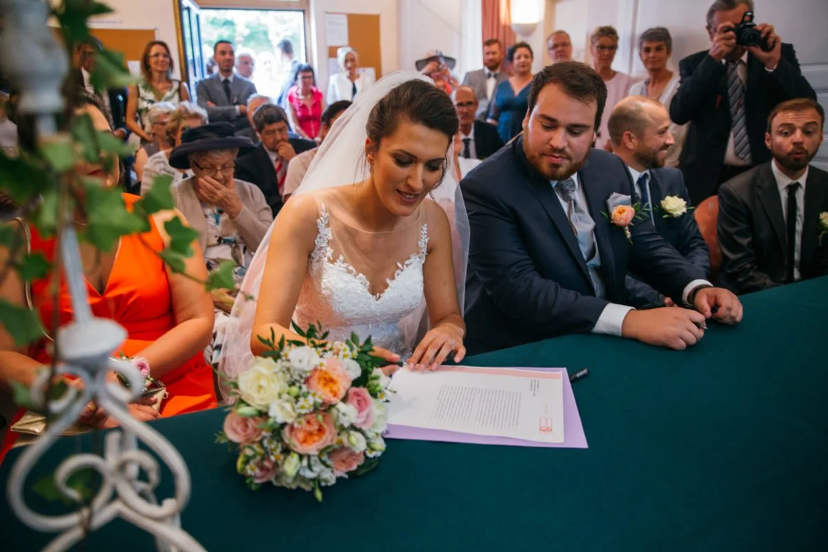Un mariage, avec un couple marié signant un document, entouré de proches et amis.