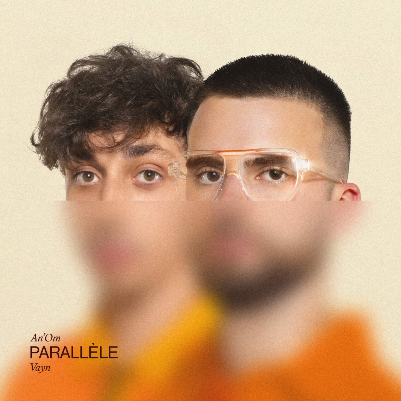 Deux hommes regardent l'objectif, l'un avec des cheveux bouclés et l'autre avec une coupe de cheveux courte et porte des lunettes. Le texte en bas à gauche indique : « An’Om PARALLÈLE Vayn ».