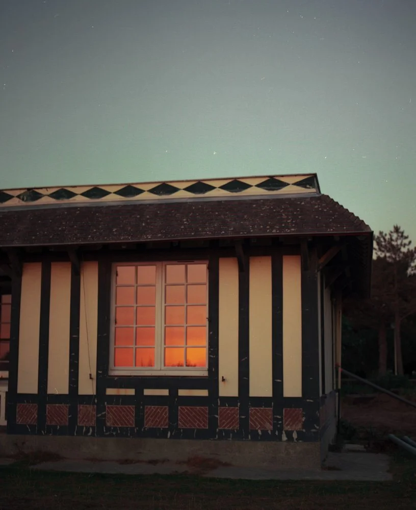 Une maison en bois avec des murs à colombages, sous un ciel étoilé, avec une fenêtre illuminée par la lumière orange à l'intérieur.