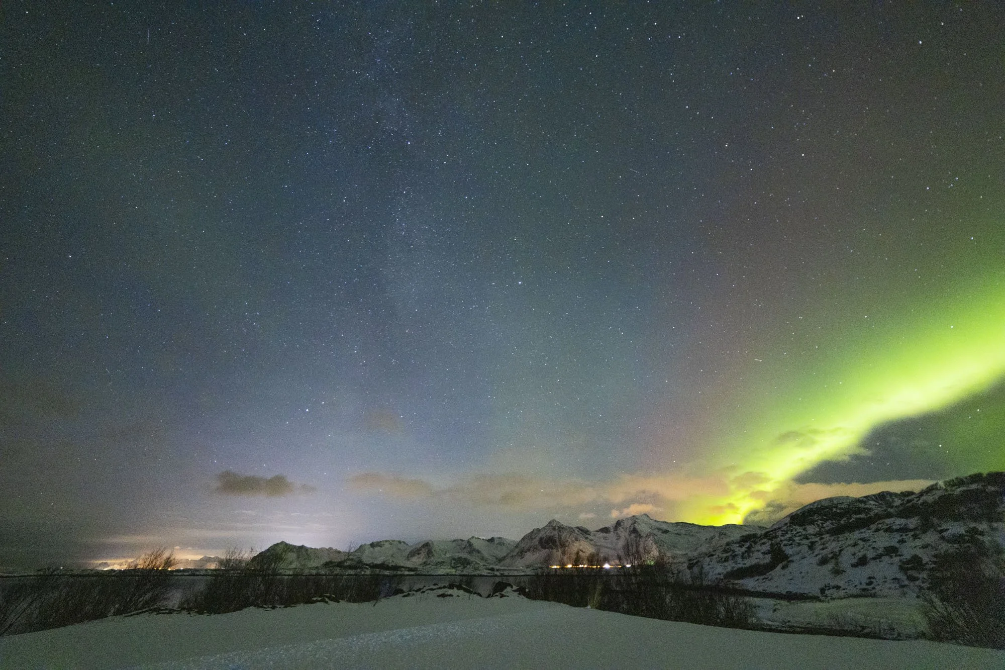 Ciel nocturne avec aurore boréale verte, montagnes enneigées et étoiles brillantes à Tromsø.