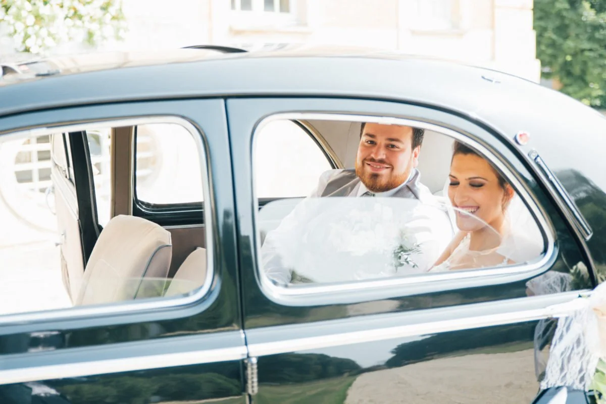 Un couple heureux assis dans une voiture ancienne, la mariée porte une robe de mariage et un voile, et tient un bouquet de fleurs.