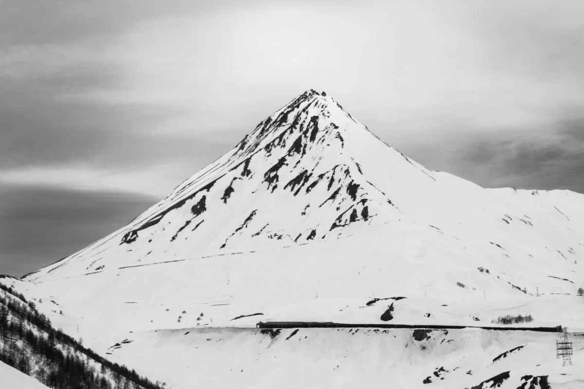 Montagne enneigée en forme de pyramide avec quelques lignes de crevasse, ciel nuageux