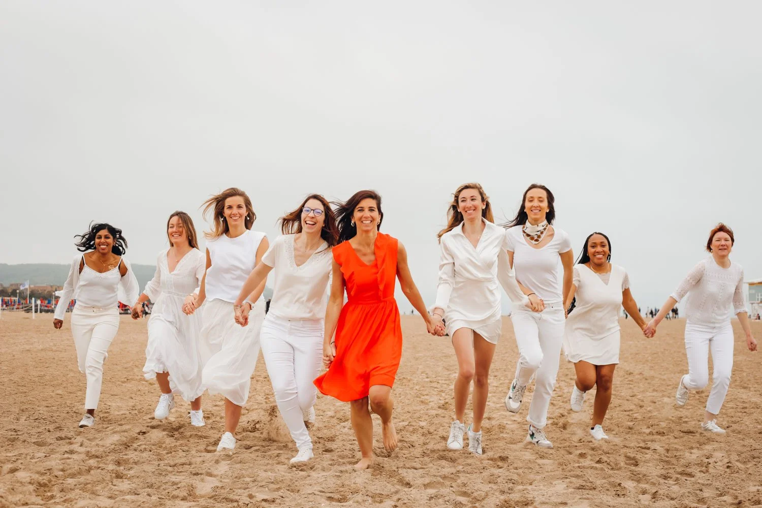 Un groupe de femmes en vêtements blancs et une femme en robe rouge, marchant joyeusement sur la plage.