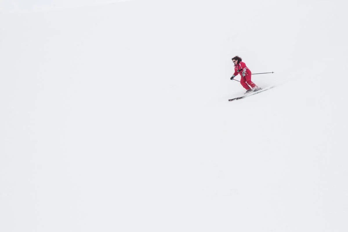 Une skieuse en rouge descend une pente enneigée dans un paysage blanc.