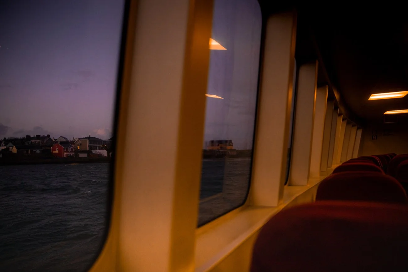 Vue depuis l'intérieur d'un ferry ou d'un bateau, montrant la mer sombre et des maisons colorées sur la côte vue à travers les fenêtres, au crépuscule ou le soir.