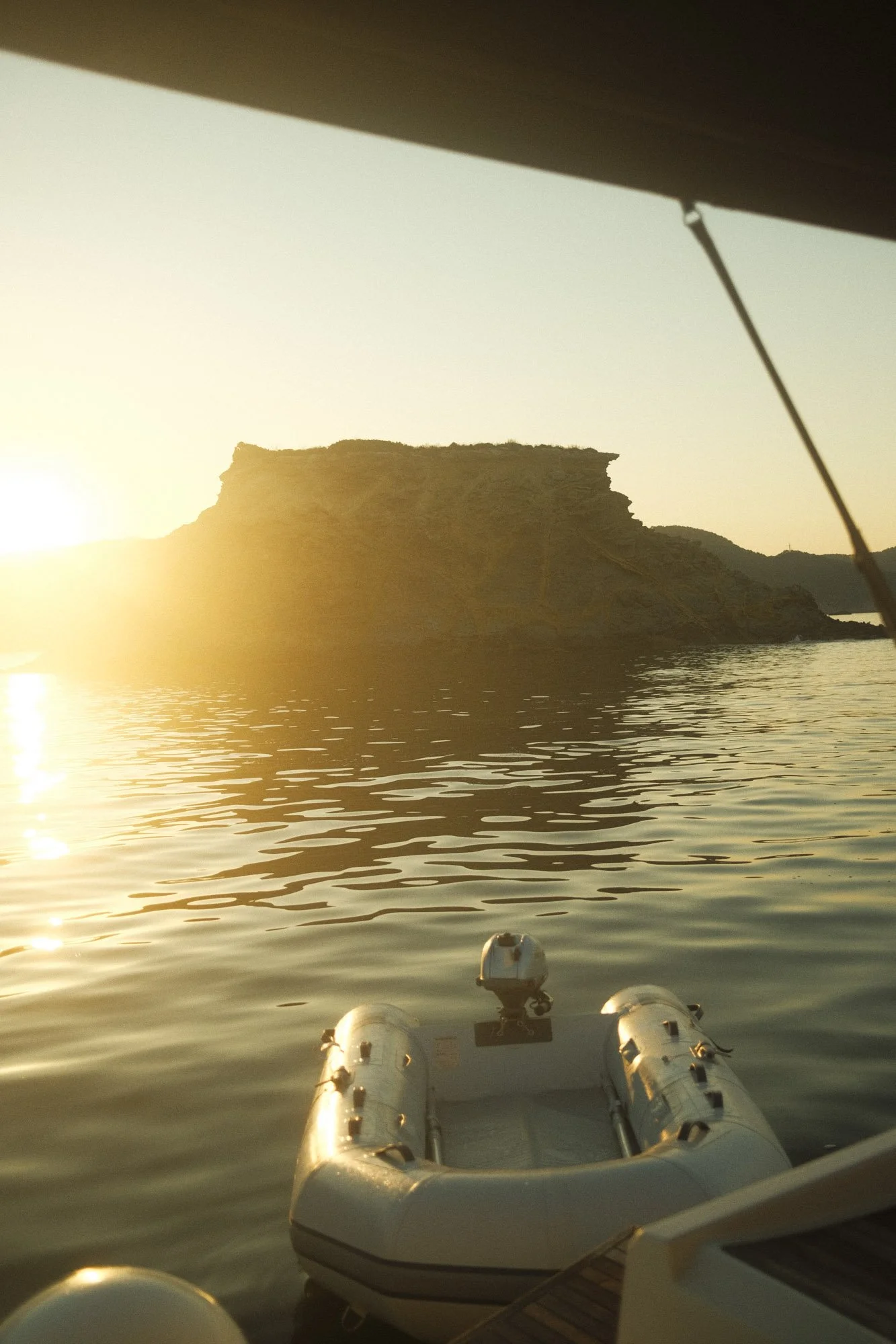 Une vue d'un plan d'eau au coucher du soleil, avec une île rocheuse en arrière-plan et un bateau gonflable blanc en premier plan à majorque