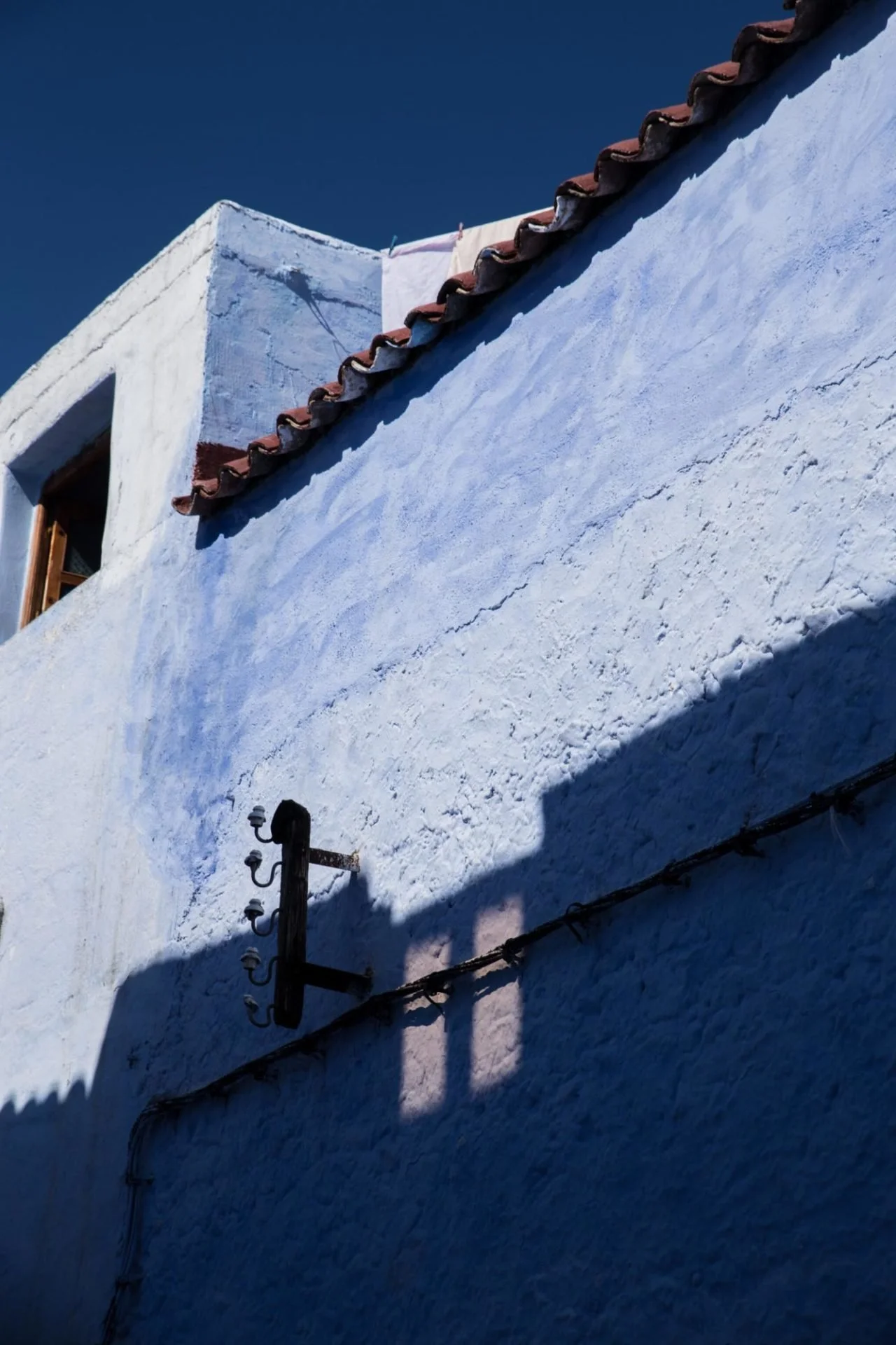 Une maison blanche avec un toit de tuiles rouges, vue de dessous contre un ciel bleu clair, avec un poteau électrique dans le premier plan.
