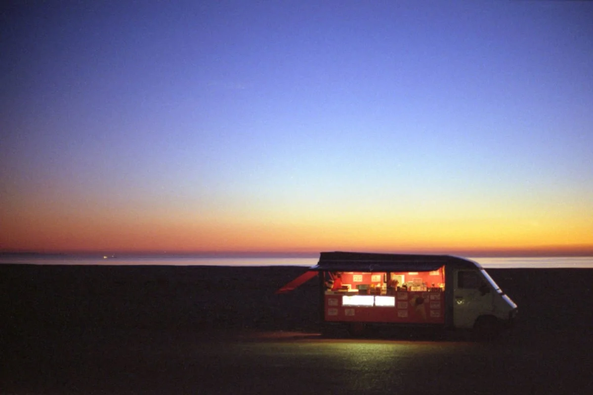 Un camion-restaurant sur une plage au coucher du soleil avec un ciel coloré.