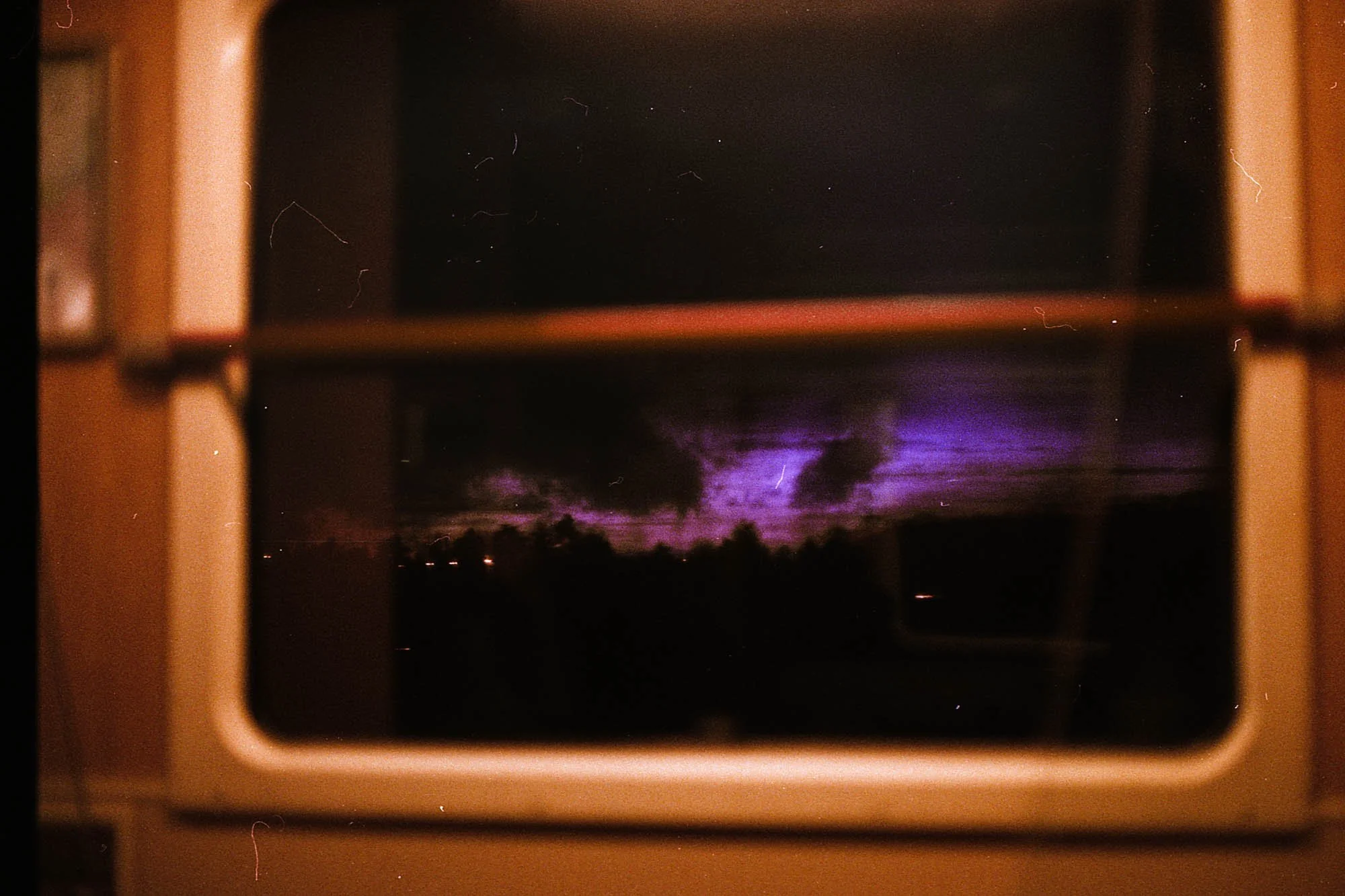 Vue d’un ciel nocturne avec des éclairs violets visibles à travers une fenêtre encadrée beige.