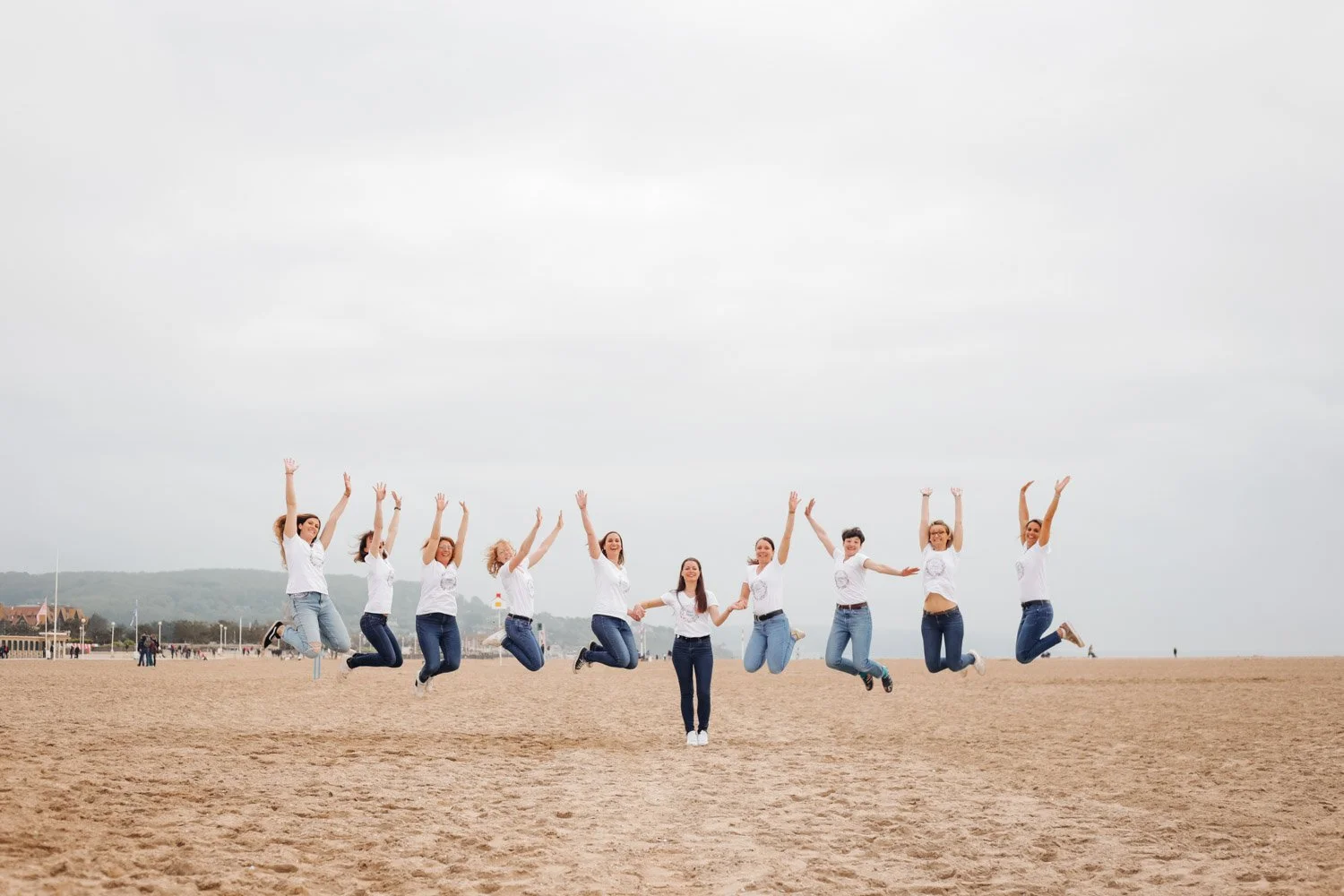 Groupe de femmes en jeans et t-shirts blancs sautant sur la plage