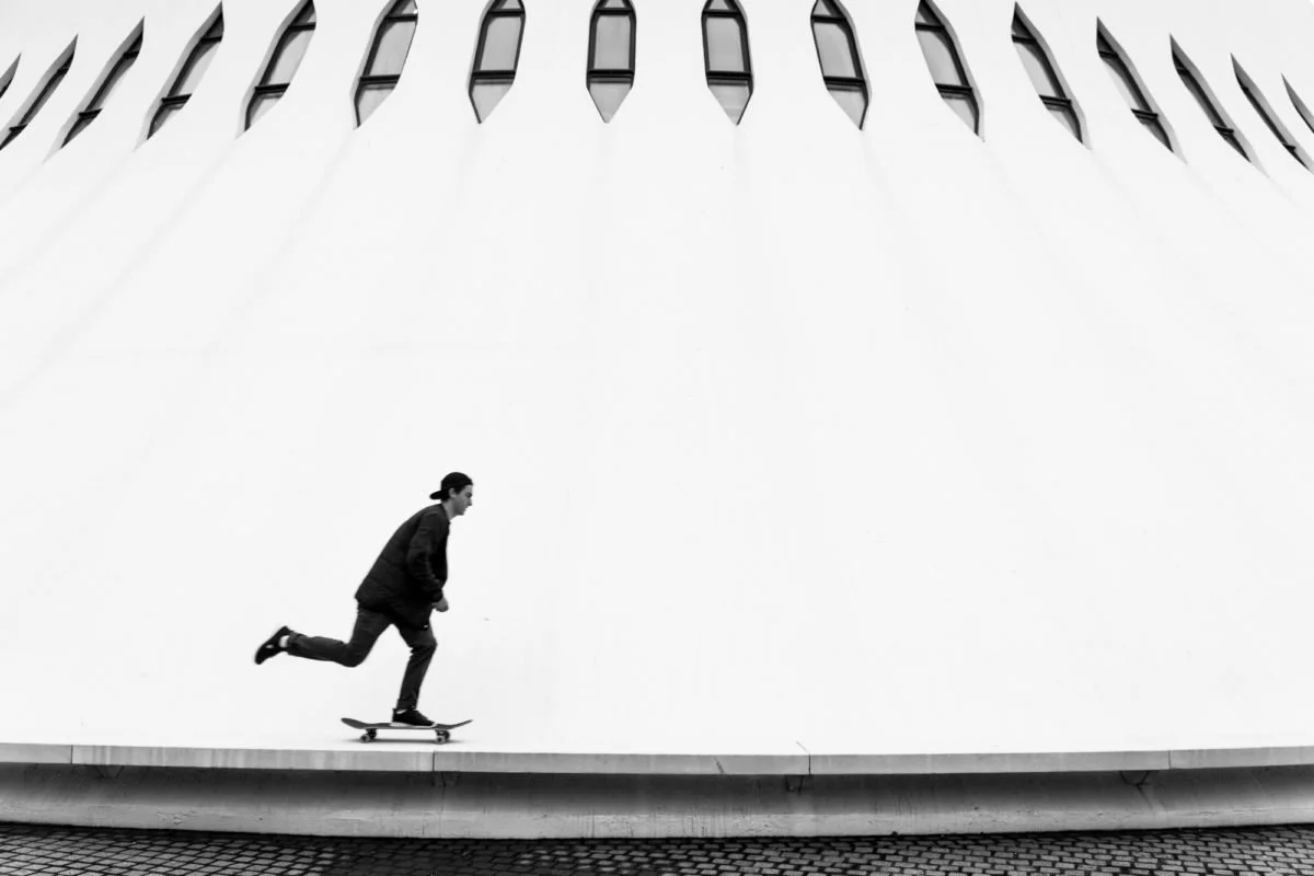 Joseph Garbaccio en sweat à capuche et casquette à l'envers fait du skateboard devant un bâtiment moderne au Havre